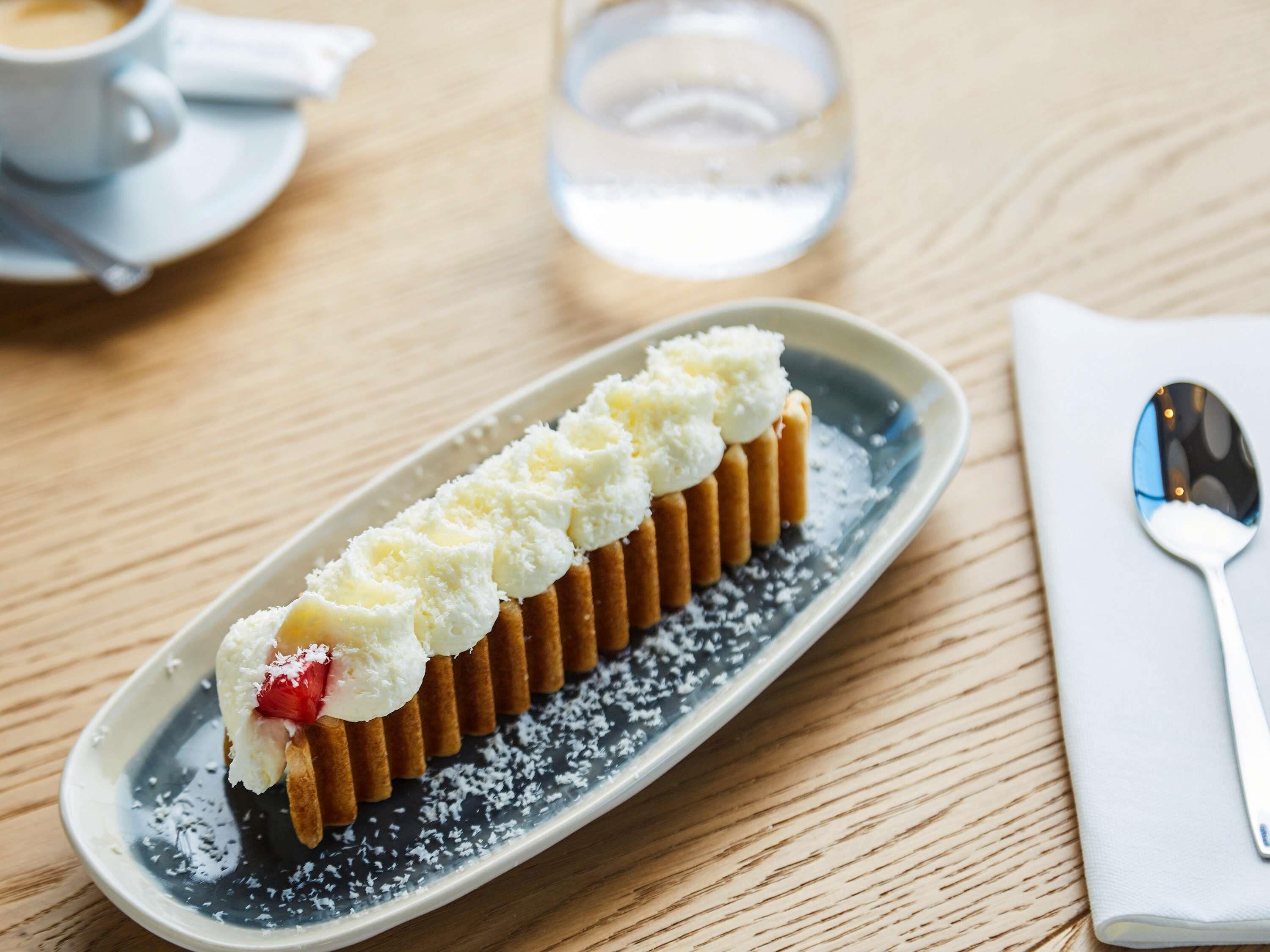 Ein Dessert auf einem Teller mit einem Löffel und einer Tasse im Hintergrund.