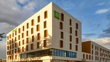 A modern hotel building with multiple floors, large windows, and a prominent green sign for ibis styles.