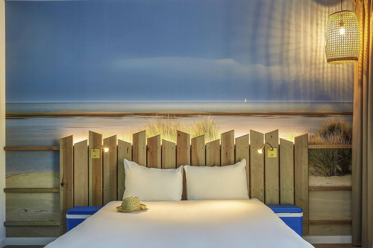 Ein Schlafzimmer mit Bett, Holz-Kopfteil und einem Wandbild mit Strandmotiv.
