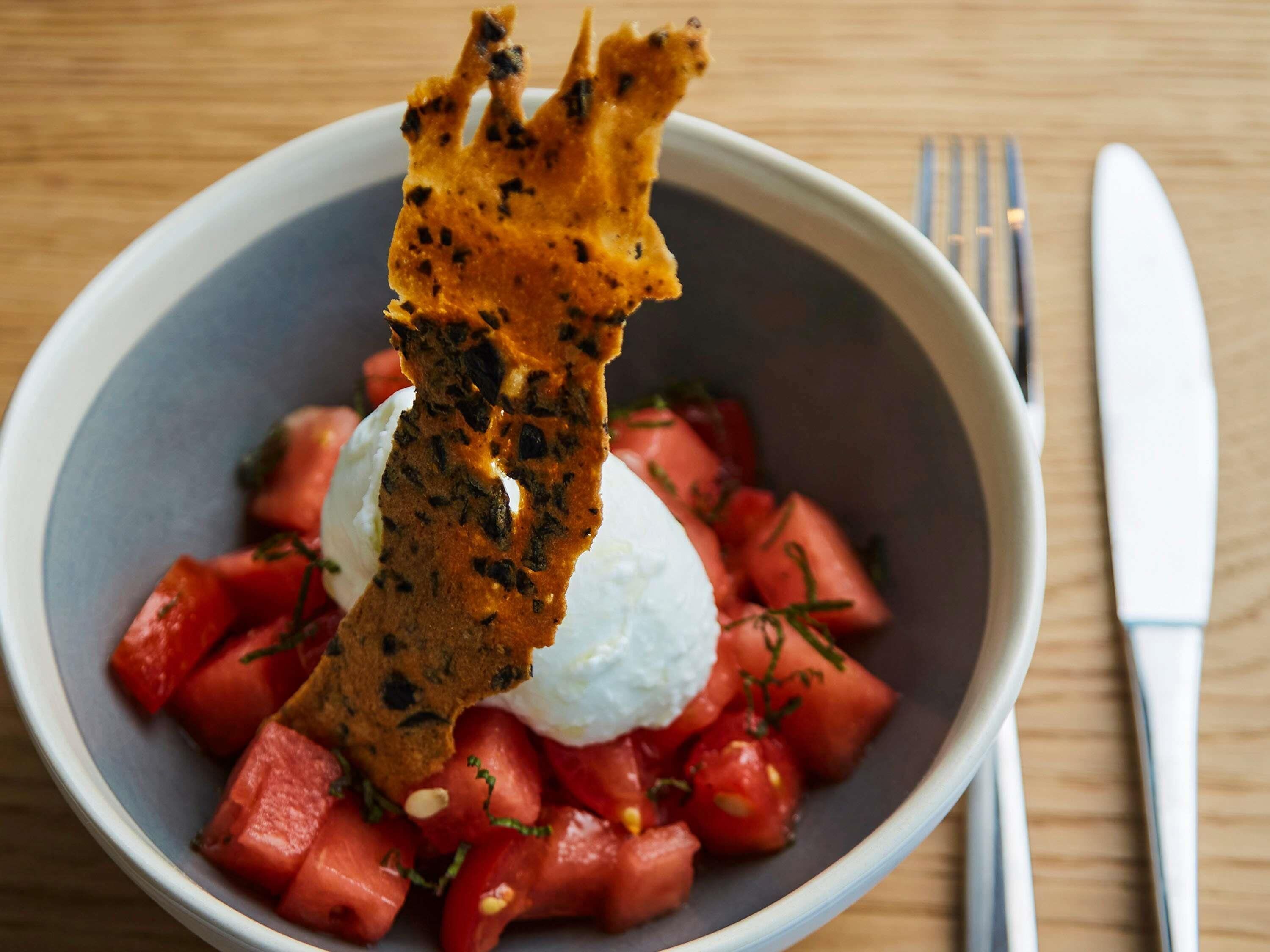 A bowl with watermelon, a dollop of cream, and a crispy item on top.
