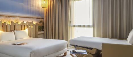 A hotel room with two beds, a sofa, a small table, and a large window with curtains.