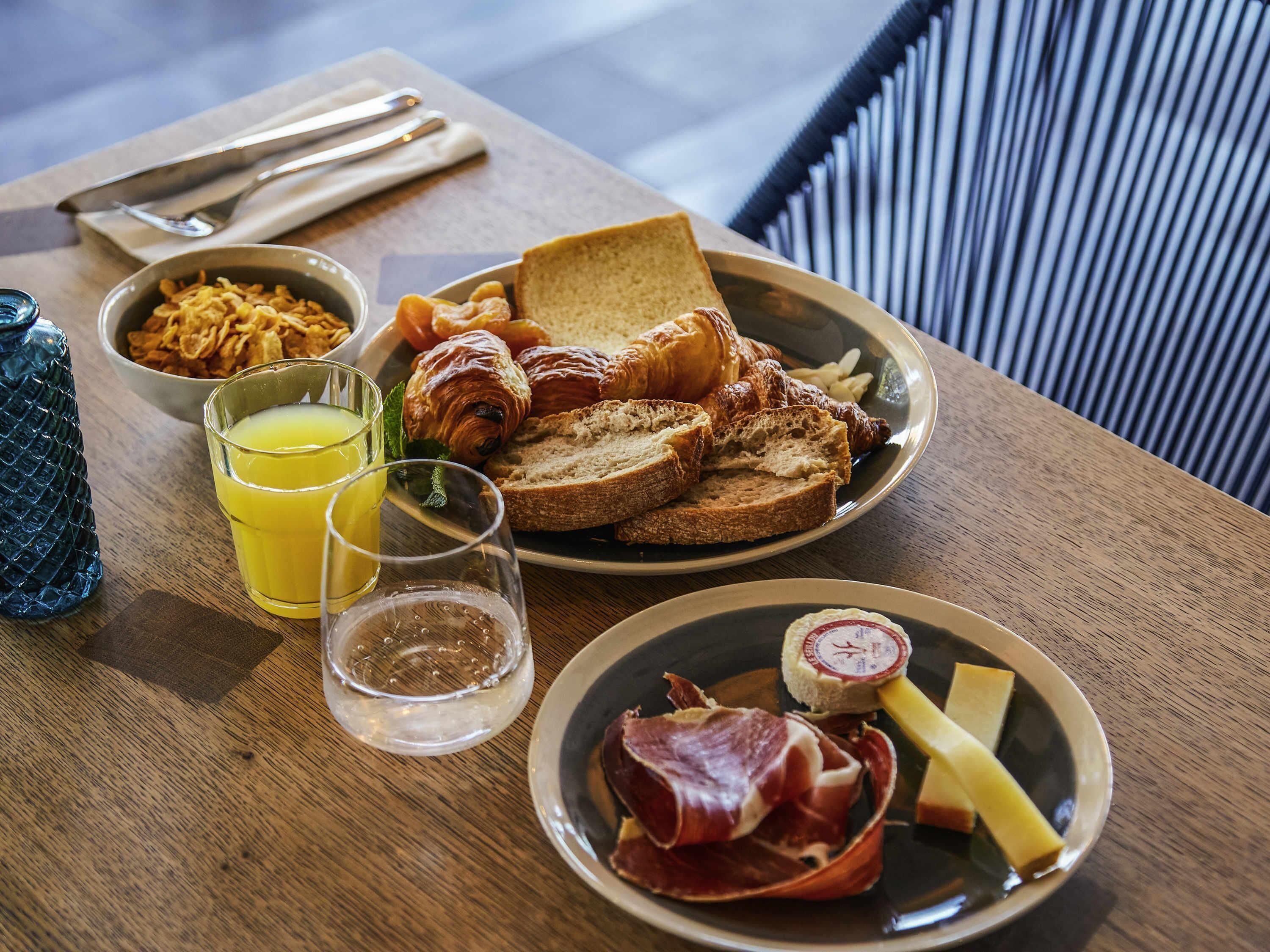A breakfast setting with toast, croissants, bacon, ham, cheese, and cereal.