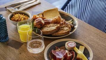 A breakfast setting with toast, croissants, bacon, ham, cheese, and cereal.