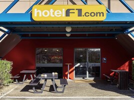 L’entrée d’un hôtel avec une façade rouge, une enseigne jaune indiquant « hotelFL.com », et un espace extérieur abrité avec des tables de pique-nique.