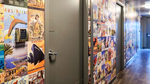 A hallway with travel posters on the walls, a door with a handle, and a wooden floor. - hotelF1 Avignon Nord (Sorgues)
