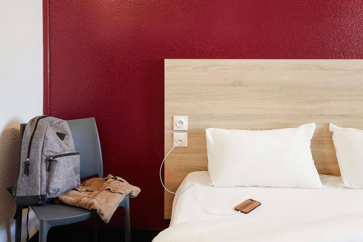 Quarto de hotel com cama, cadeira, uma mochila e cabeceira de madeira.