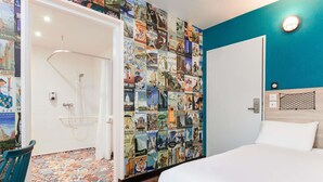 A hotel room with a bed, a shower, a wall decorated with travel posters, and a blue accent wall. - hotelF1 Avignon Nord (Sorgues)