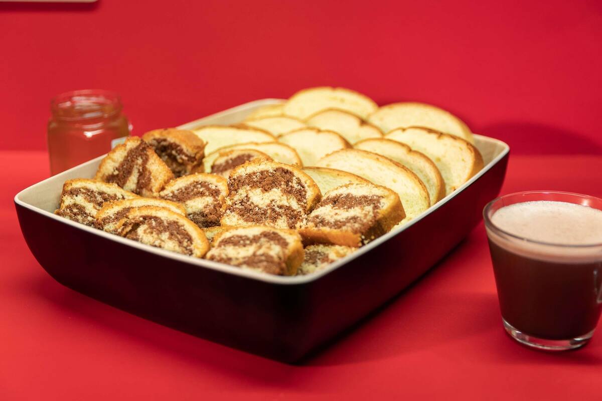 Uma bandeja com fatias de pastelaria e um copo de bebida escura sobre uma mesa vermelha.