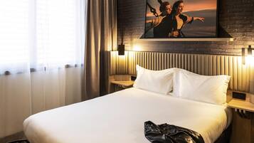 A hotel room with a bed, a headboard, a wall-mounted picture, and a window with curtains.