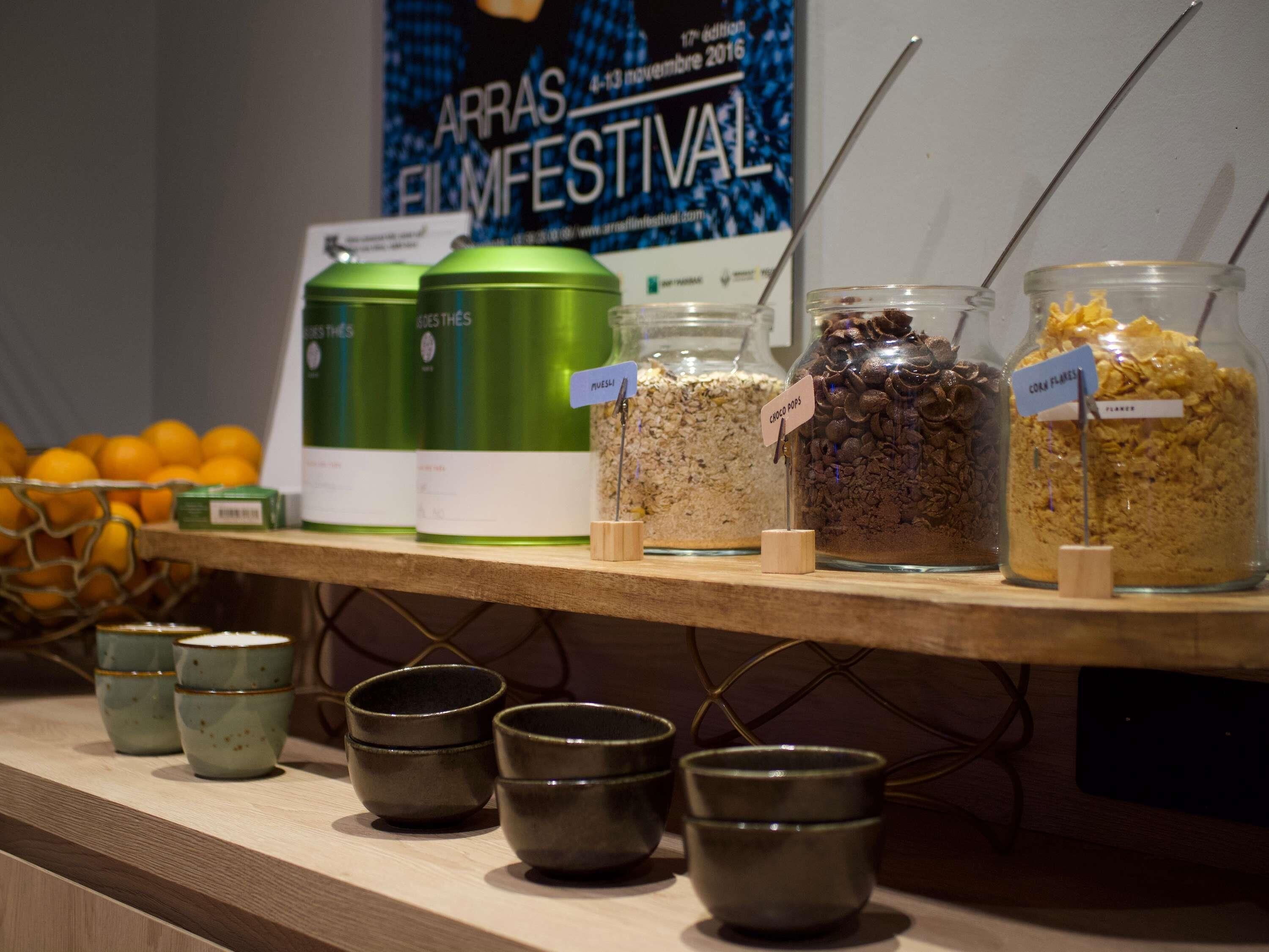 A snack bar with jars labeled with food items, a poster in the background, and a basket of oranges.
