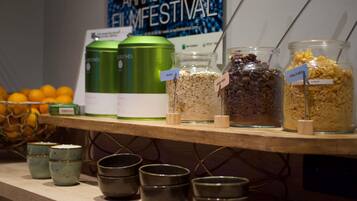 A snack bar with jars labeled with food items, a poster in the background, and a basket of oranges.