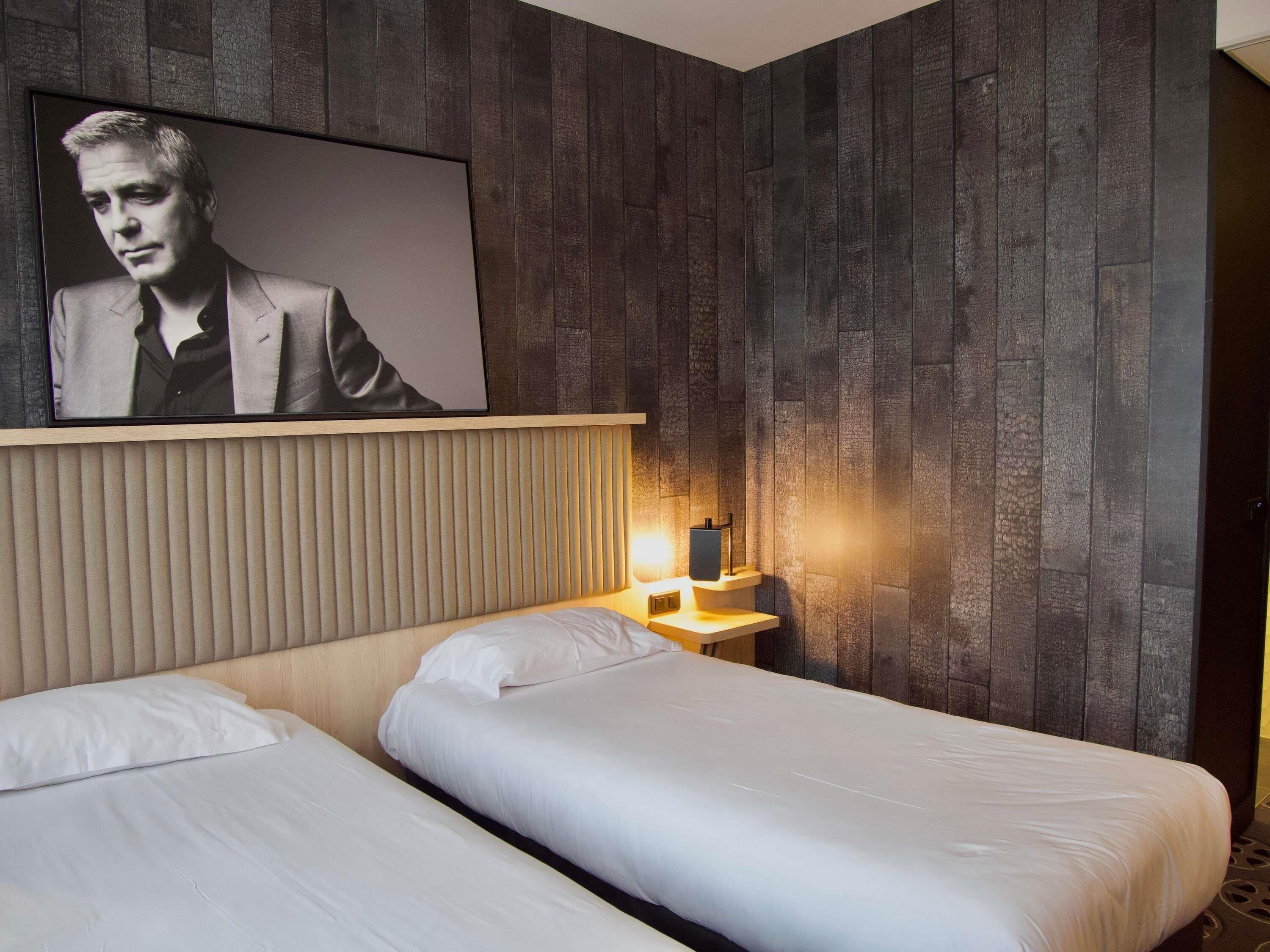 Une chambre d’hôtel avec un mur en bois, un portrait encadré, une table de chevet avec une lampe et deux lits.