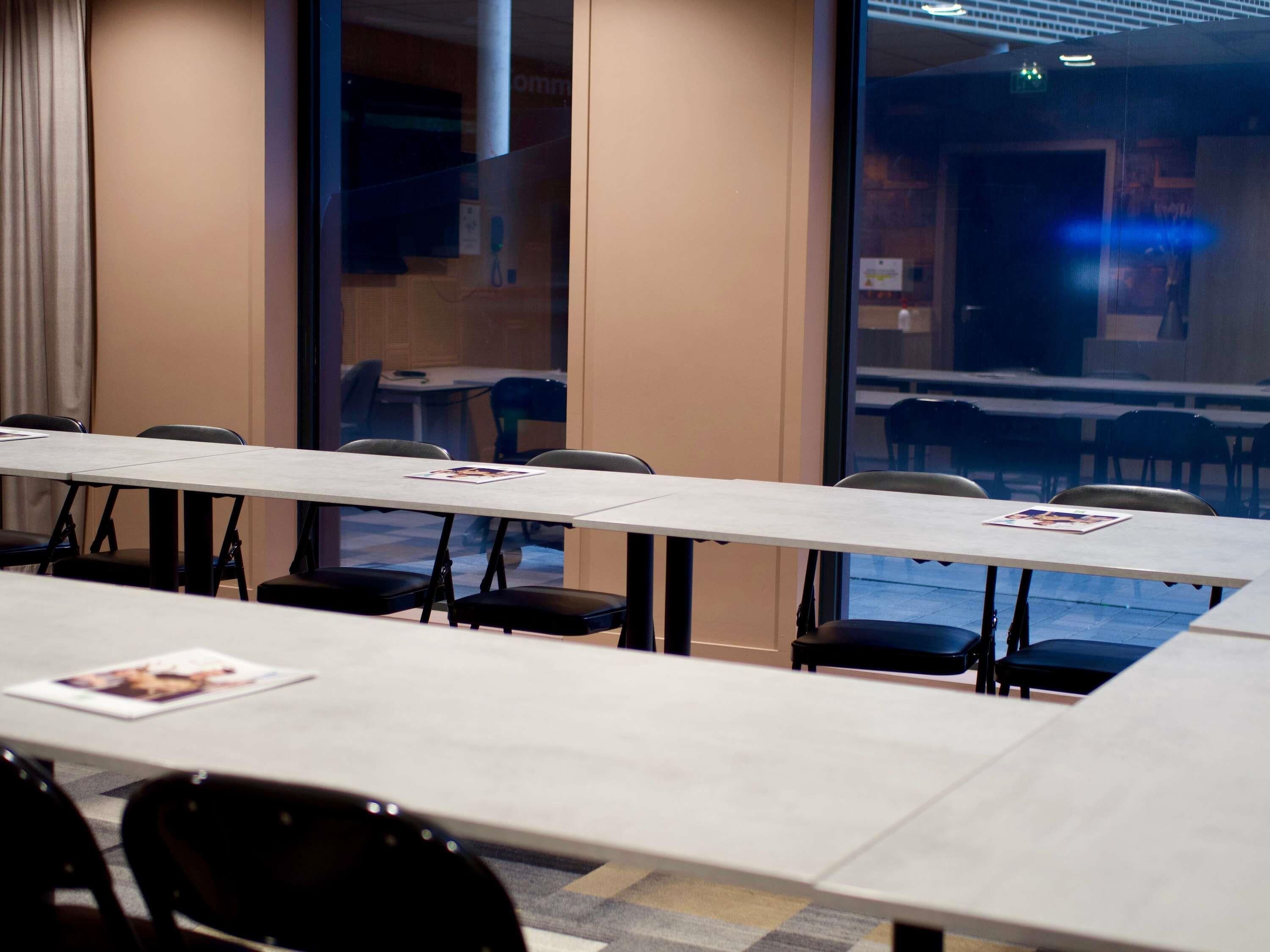 Une salle de conférence avec une longue table et des chaises, de grandes fenêtres et une vue sur l’extérieur.