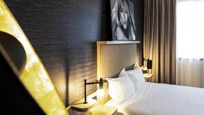 Una habitación de hotel moderna con pared de ladrillo, una cama grande, un televisor montado y una mesita de noche con lámpara.
