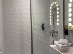 A modern bathroom with a hexagonal tile wall, a glass-enclosed shower with lights, a white sink, and a towel rack.
