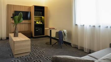 A hotel room with a sofa, a small table, a TV, a minibar, and a window with curtains.