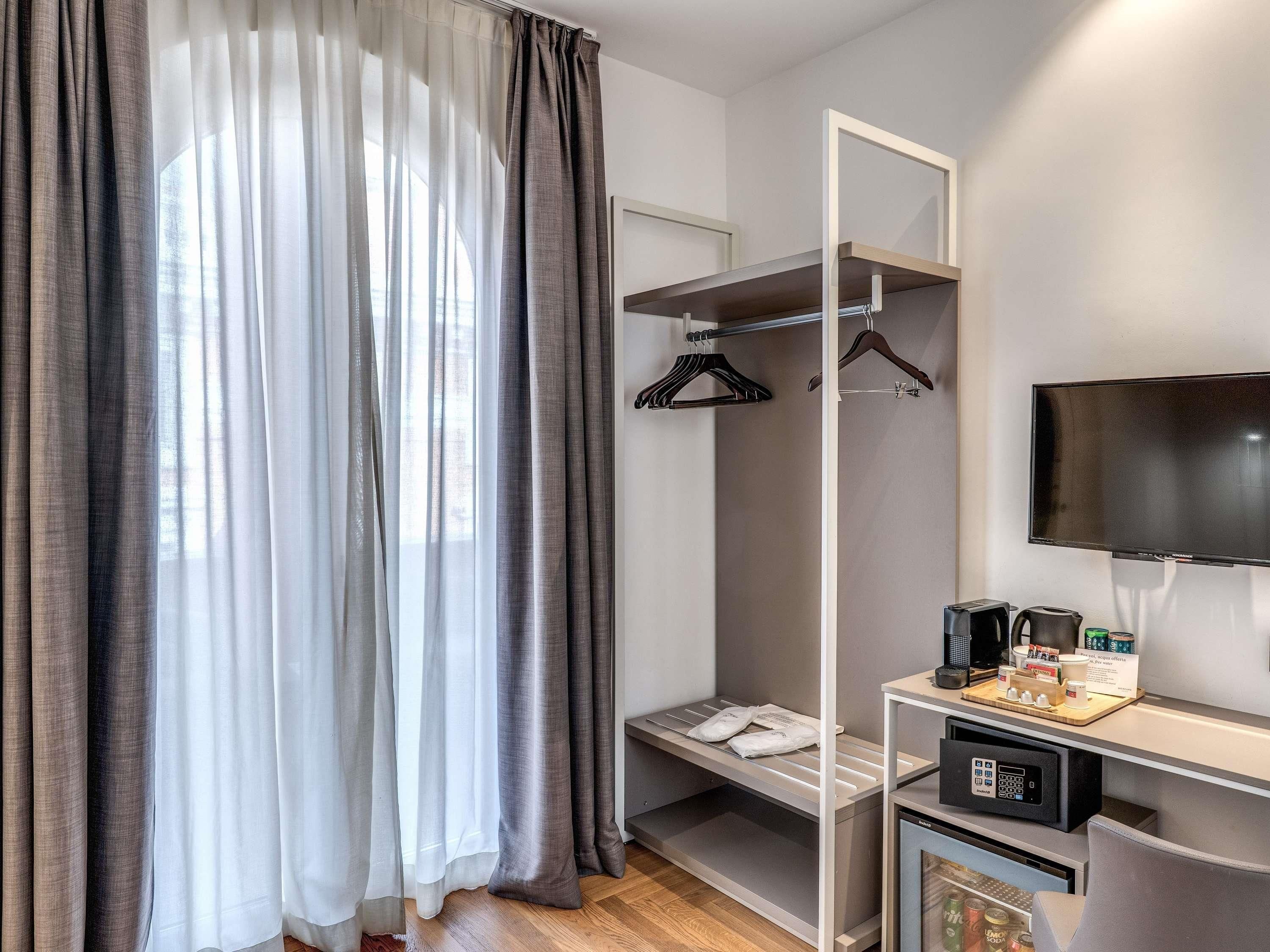 Habitación de hotel con cama, televisión, cafetera y repisas con artículos de aseo.