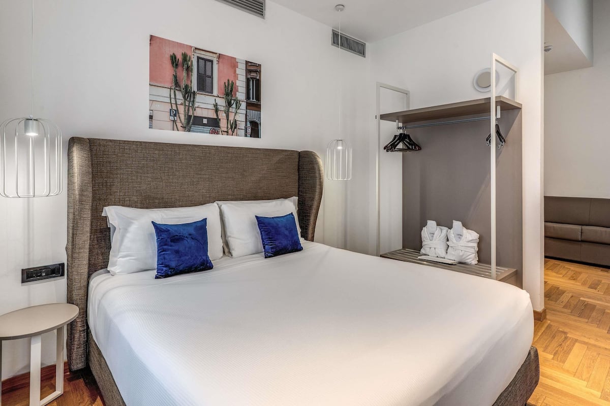 Ein modernes Hotelzimmer mit einem großen Bett, einem Nachttisch, einem Kleiderschrank und einem Gemälde an der Wand.
