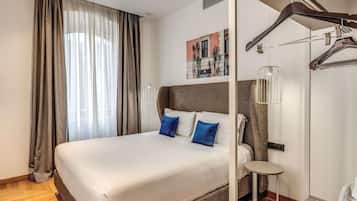 Habitación de hotel con una cama grande, una mesita pequeña, un perchero y un cuadro en la pared.