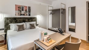 A modern hotel room with a large bed, a desk with a phone and toiletries, a mirror, and a shower area.
