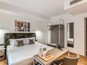 Quarto de hotel moderno com uma cama grande, uma escrivaninha com telefone e artigos de higiene, um espelho e uma área de chuveiro.