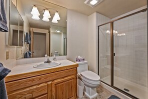 Une salle de bain avec un meuble-lavabo en bois, un évier, des toilettes, une cabine de douche en verre et un grand miroir avec éclairage.