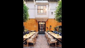 A courtyard with wooden tables and wicker chairs, a brick wall, and a glass ceiling. - Amerikalinjen (Oslo)