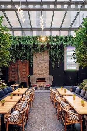Ein Restaurant mit Glasdecke, sechseckigen Fliesen, Holztischen und -stühlen sowie einer Ziegelwand mit Bepflanzung.