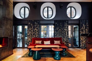 Eine moderne Lounge mit einem roten Sofa, runden Tischen und drei großen Fenstern.