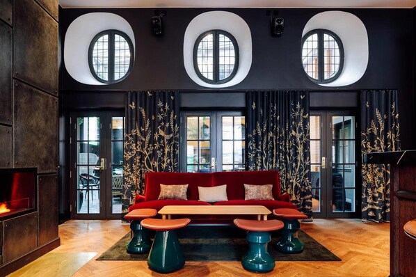 A modern lounge with a red sofa, round tables, and three large windows. - Amerikalinjen (Oslo)