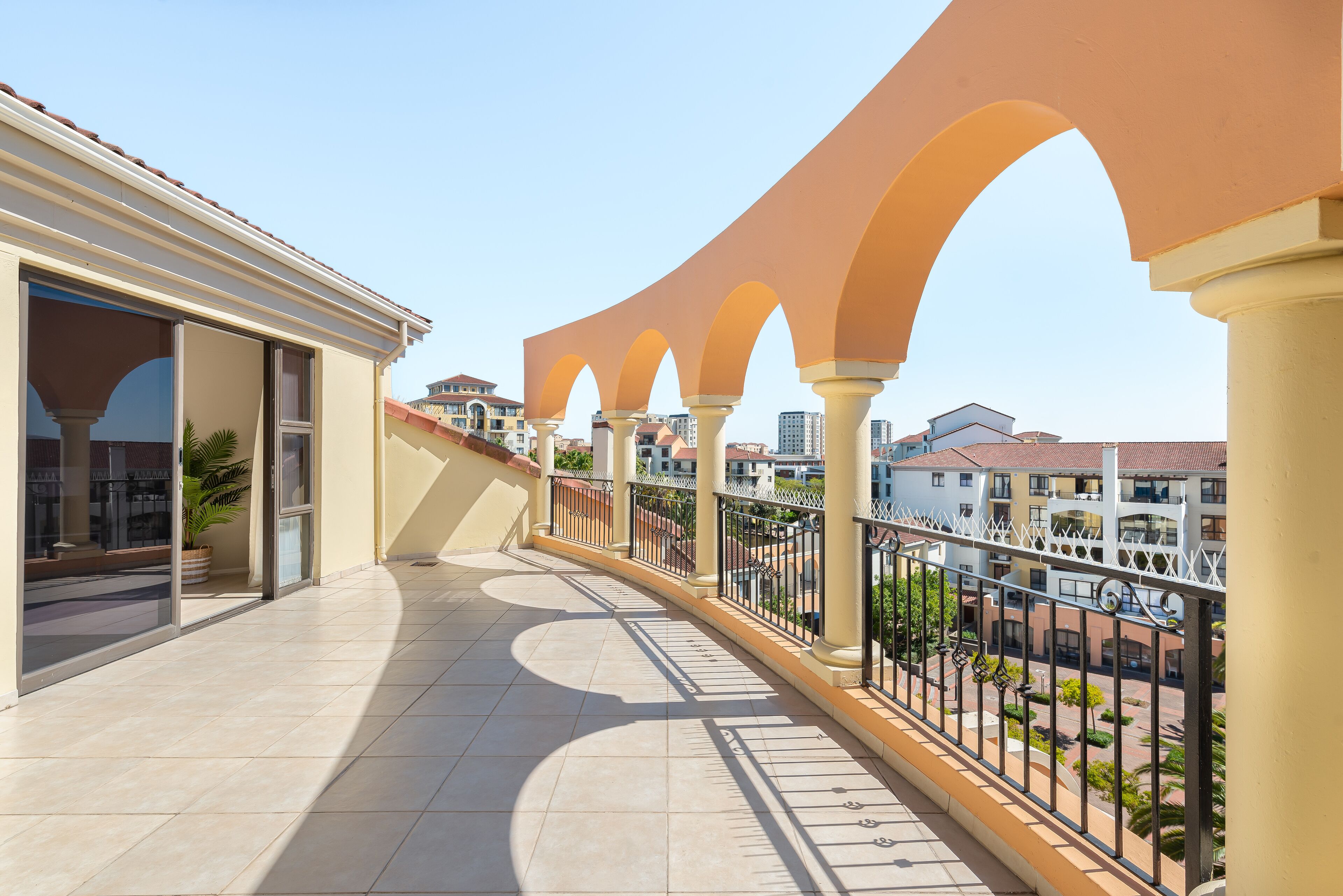 A balcony with a tiled floor, a potted plant, and a view of surrounding buildings.