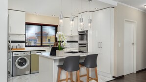 A modern kitchen with a built-in washer and dryer, a large island with bar stools, and pendant lighting. - Island Club 410 (Cape Town)