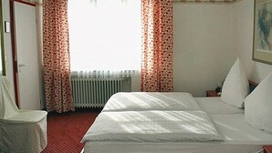 Ein Schlafzimmer mit Bett, Sessel, Heizkörper und Vorhängen.