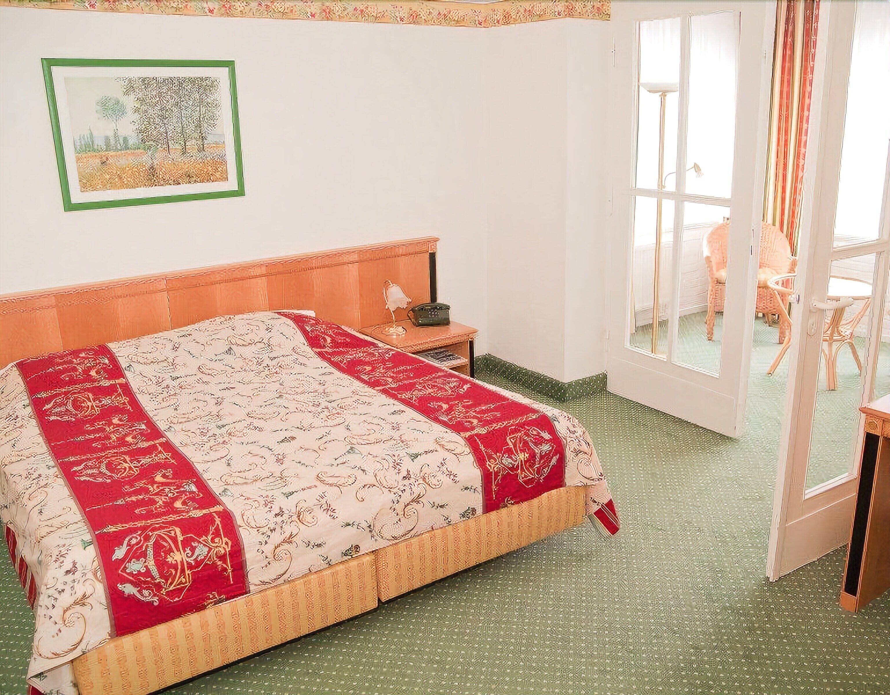 Een kamer met een bed, een nachtkastje, een lijst aan de muur en een uitzicht door een deur.