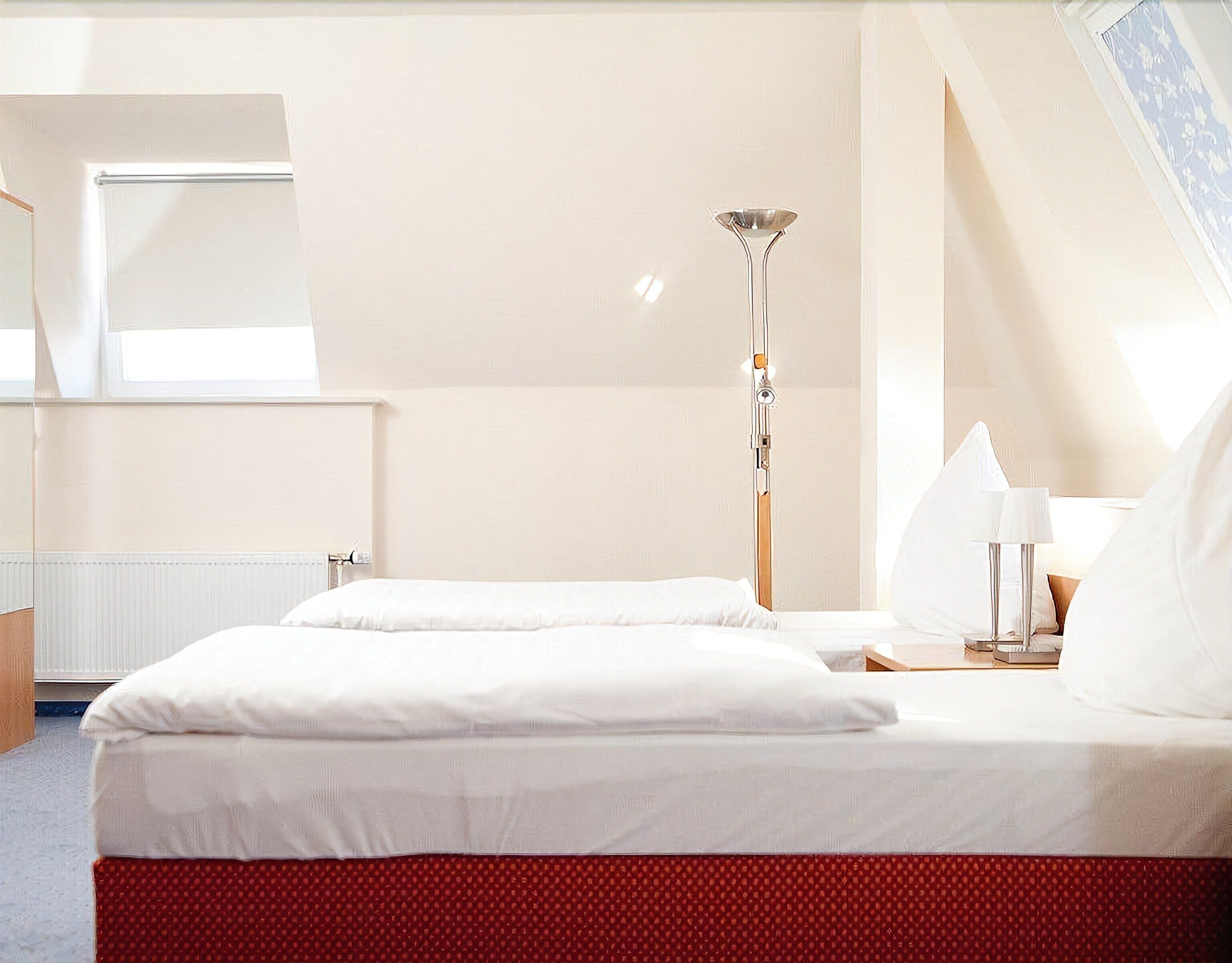 Ein Hotelzimmer mit zwei Betten, einem Nachttisch mit Lampe, einem Heizkörper und einem Fenster mit Blick.
