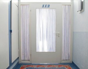 Ein Flur mit einer Tür, auf der '112' steht, einer blauen Wand und einem gemusterten Teppich.