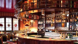 Eine Bar mit einer gebogenen Theke, Ledersitzgelegenheiten und einer Auswahl an Flaschen und Gläsern.