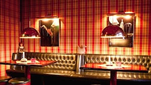Ein Restaurantinnenraum mit roter Karo-Tapete, einer Lederbank und Barhocker.