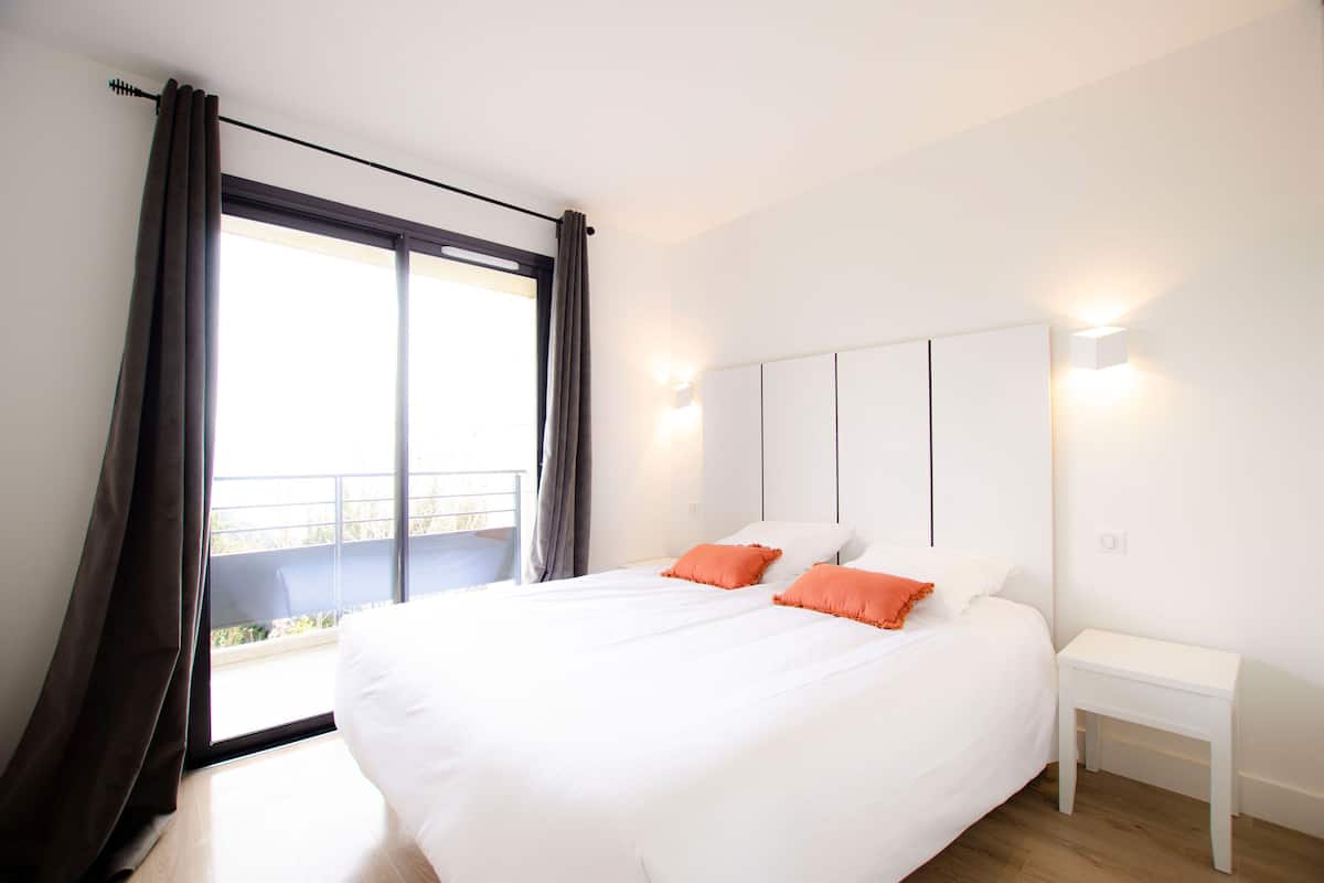 Un dormitorio moderno con una cama grande, ropa de cama blanca y vistas a un balcón.
