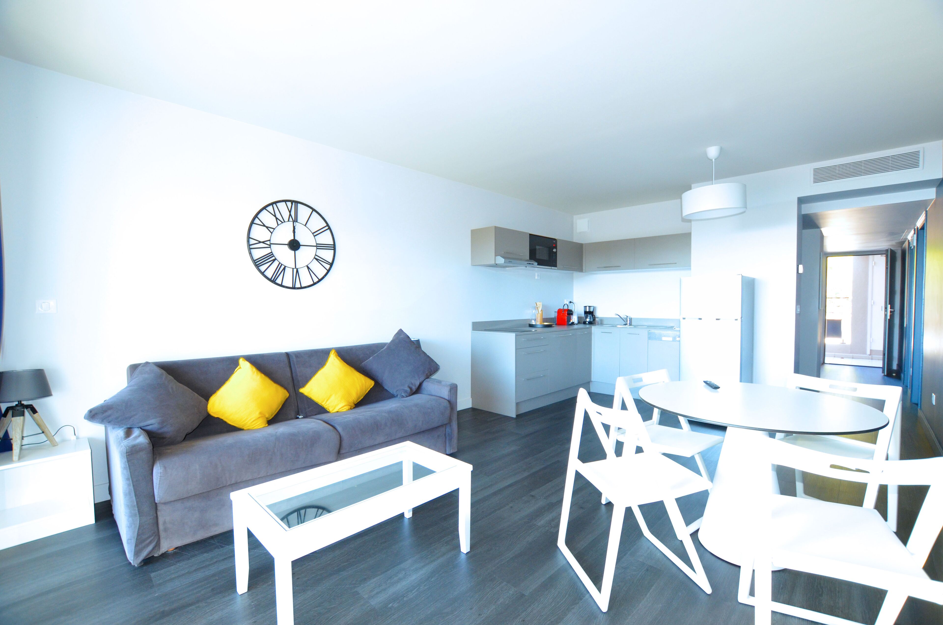 A modern living room with a grey sofa, yellow pillows, a white coffee table, and a dining area with white chairs and a round table.