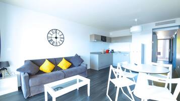 A modern living room with a grey sofa, yellow pillows, a white coffee table, and a dining area with white chairs and a round table.
