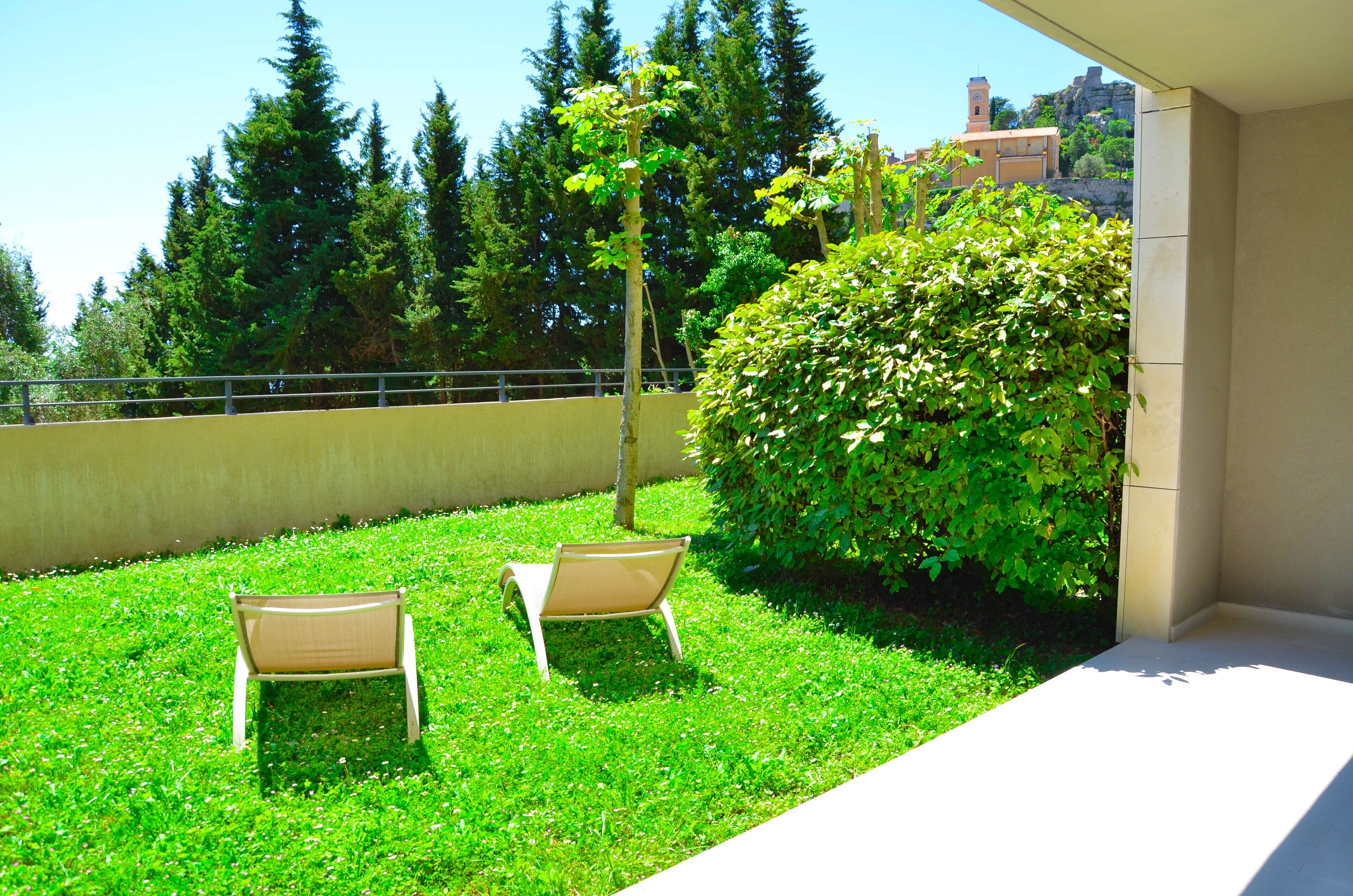 Un balcon avec deux chaises, une haie et une vue sur les arbres et les bâtiments.