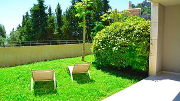 Un balcon avec deux chaises, une haie et une vue sur les arbres et les bâtiments.