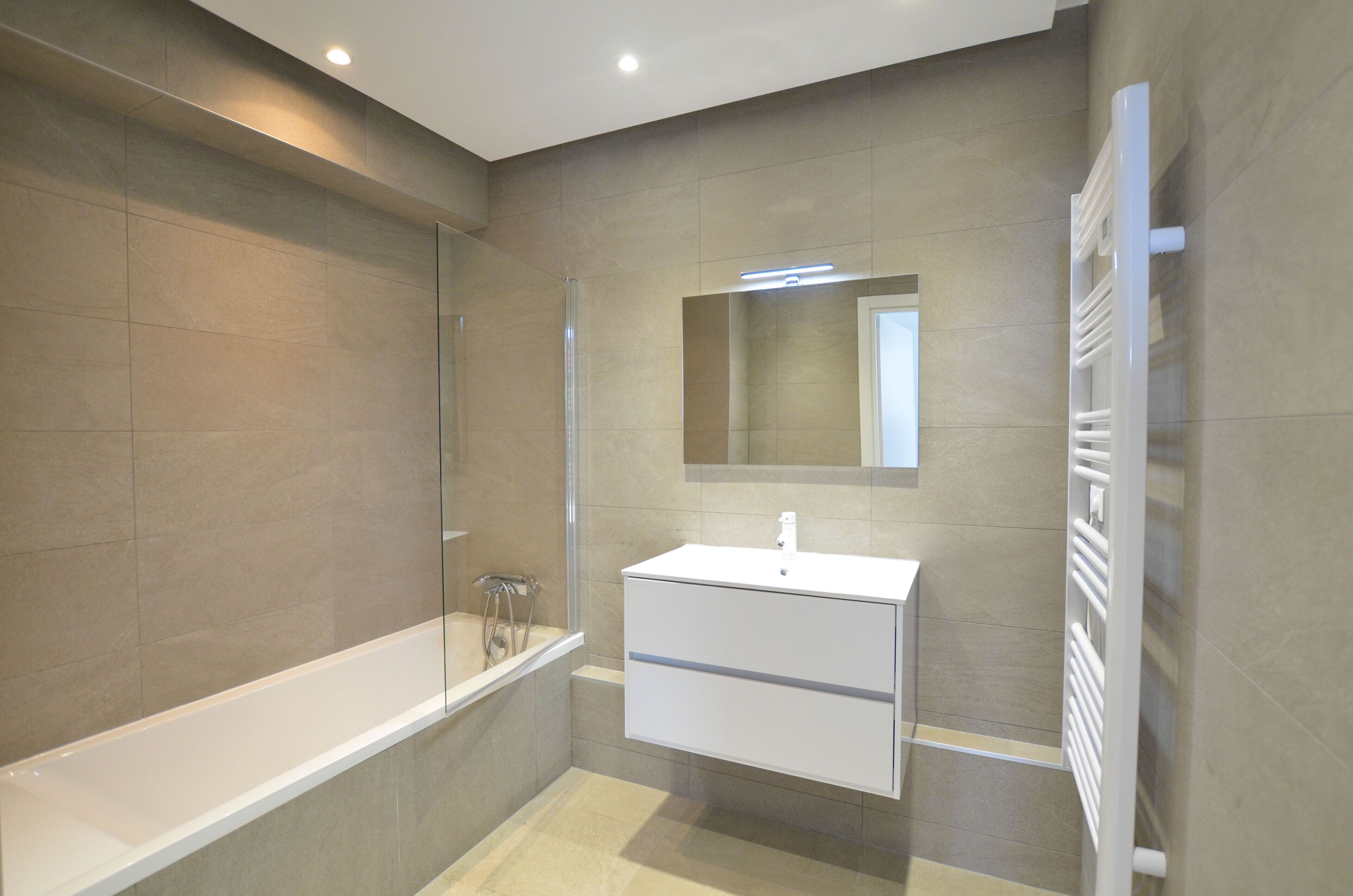 Un bagno moderno con una vasca, un mobile lavabo con specchio e un porta asciugamani.