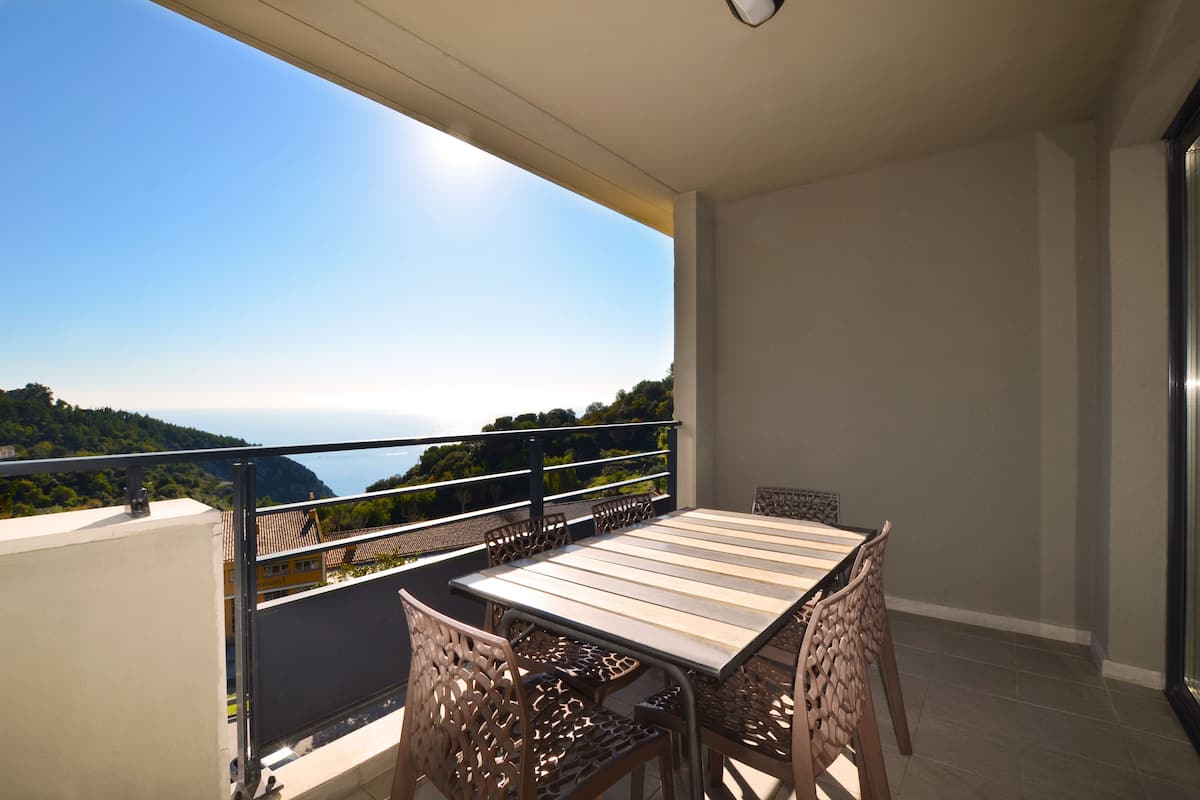 Un balcón con mesa y sillas, con vistas panorámicas de la costa y colinas.