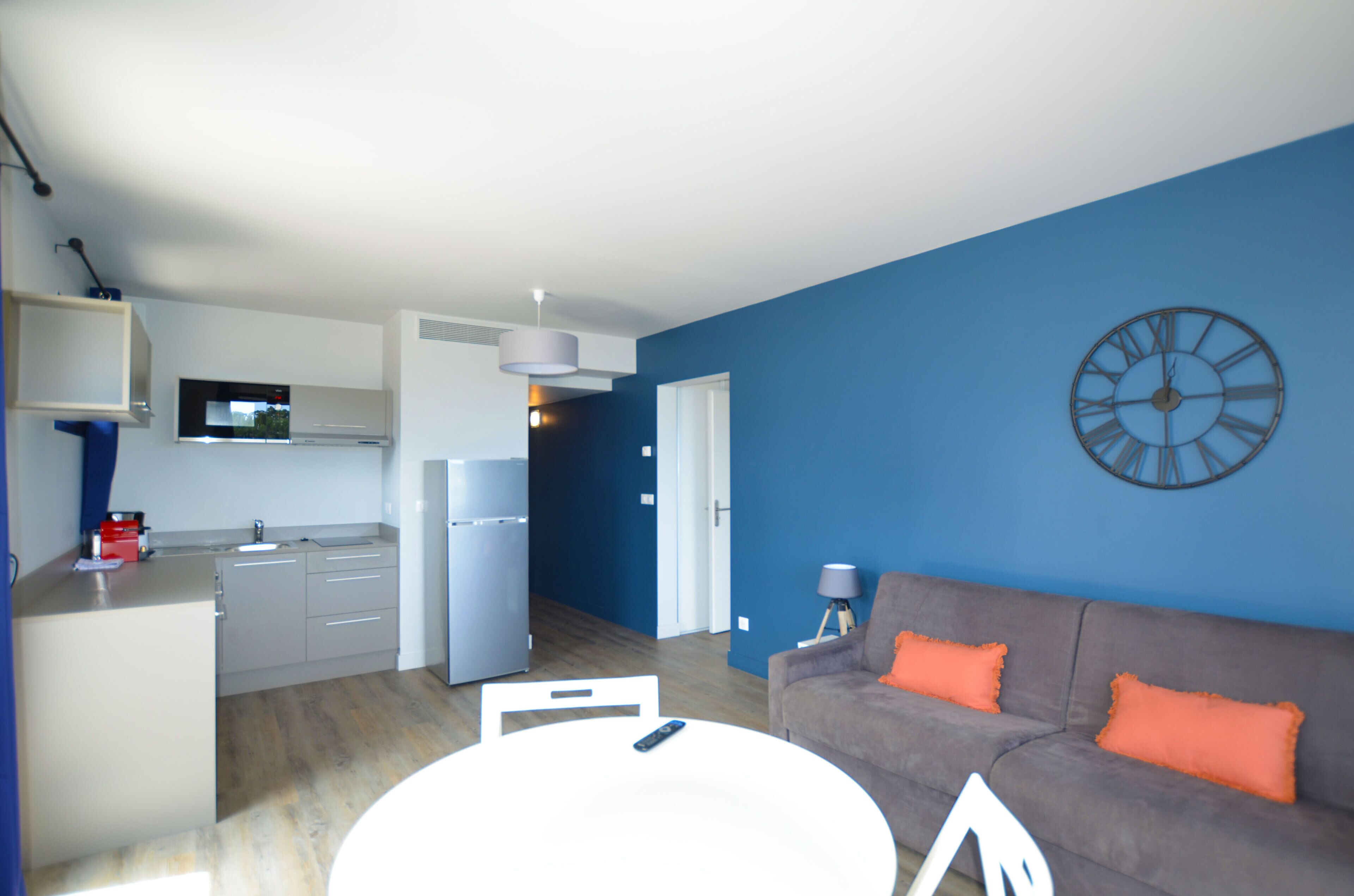 A modern living space with a kitchen, dining area, and a blue accent wall.