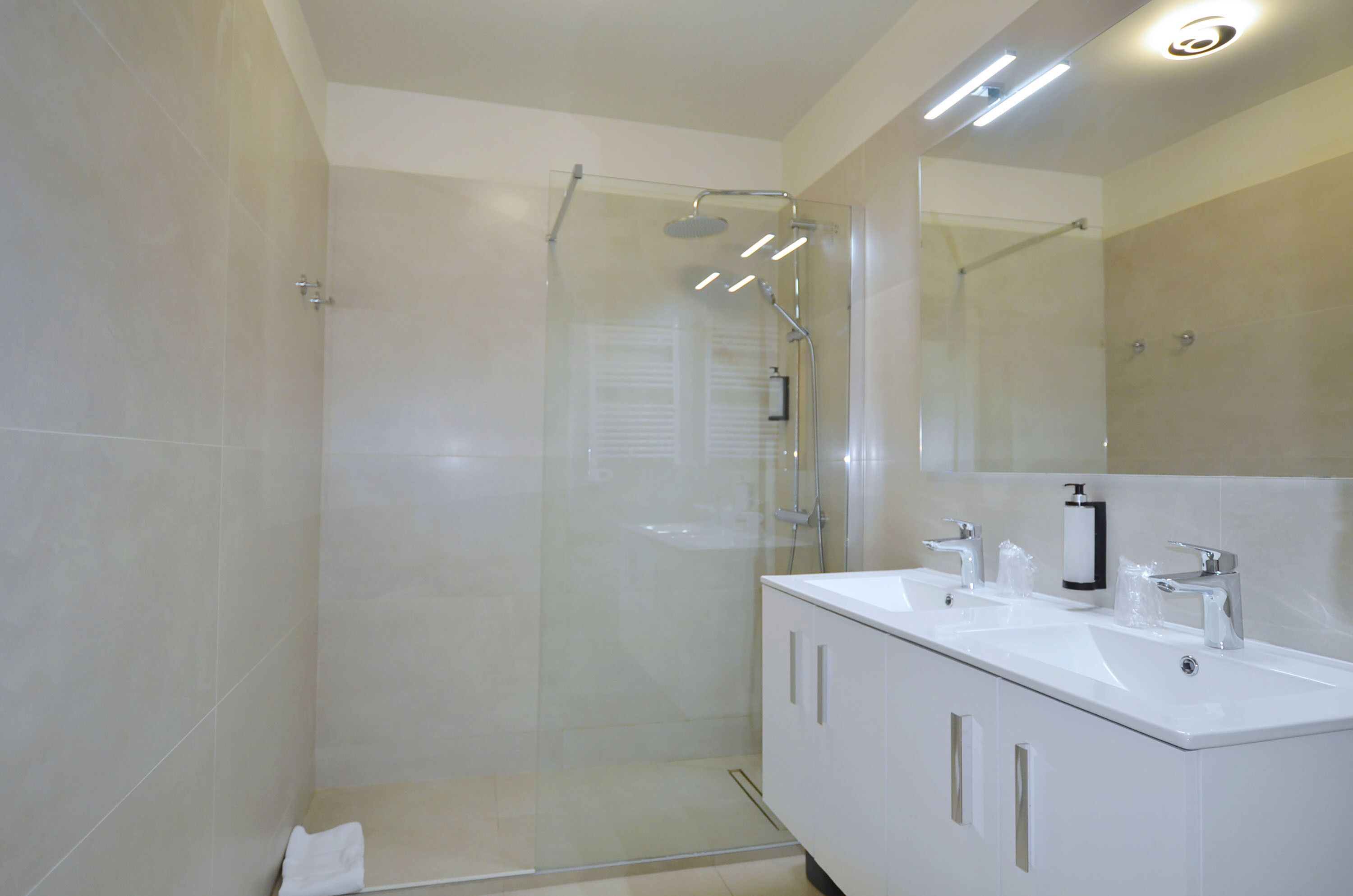 A modern bathroom with a glass-enclosed shower, a white vanity with two sinks, and a large mirror above the vanity.