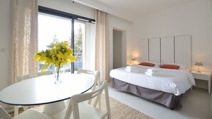 A modern hotel room with a bed, bedside tables, a round dining table, and chairs.