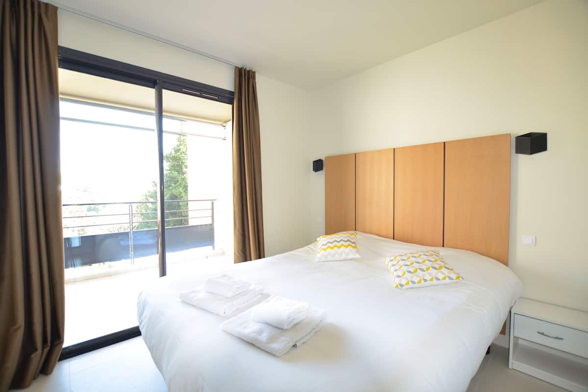 Habitación de hotel con una cama grande, dos almohadas, una mesita de noche y vistas al exterior.