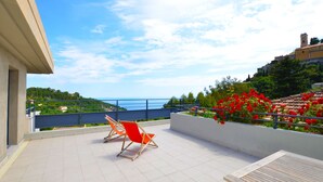 A terrace with a view of the sea, a red chair, and a wooden table.